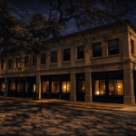 Nighttime view of a historic two story corner building in downtown Savannah, with tall windows glowing warmly from inside. Oak branches cast shadows across the façade and street beneath a starry sky.