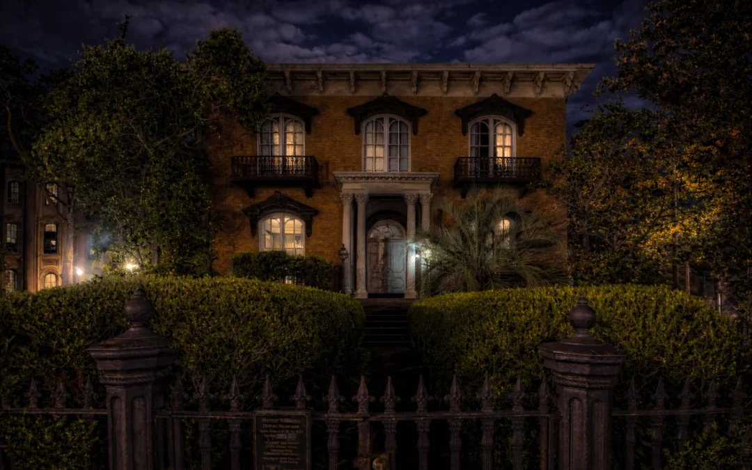 Mercer-Williams House Museum in Savannah at night with illuminated windows, wrought iron fence, and manicured hedges